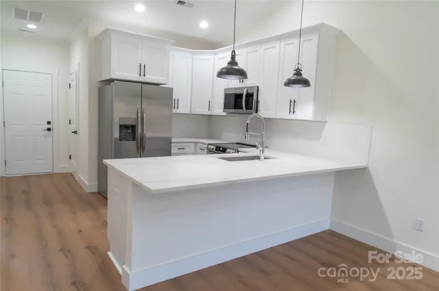 a kitchen with stainless steel appliances a refrigerator a sink dishwasher a stove and white cabinets with wooden floor