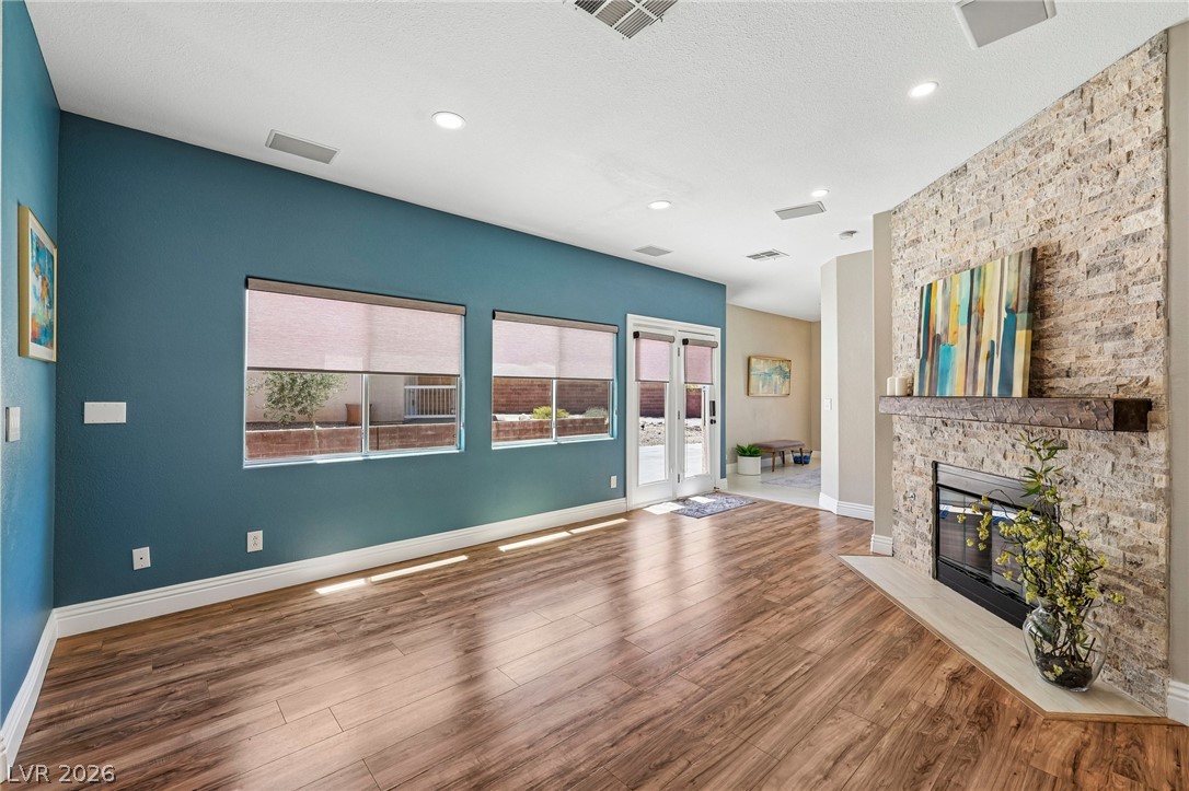 1176 Butternut Ranch Court Henderson, NV 89052 - Photo 6 of 60 Rich hardwood-style flooring extends across this vibrant living area, anchored by a textured stone fireplace.