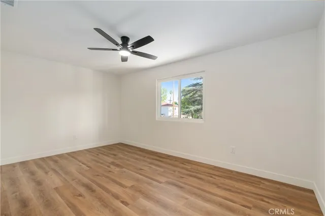 an empty room with wooden floor ceiling fan and windows