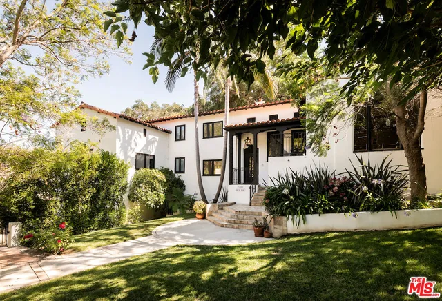 a view of a white house with a big yard and potted plants and large trees