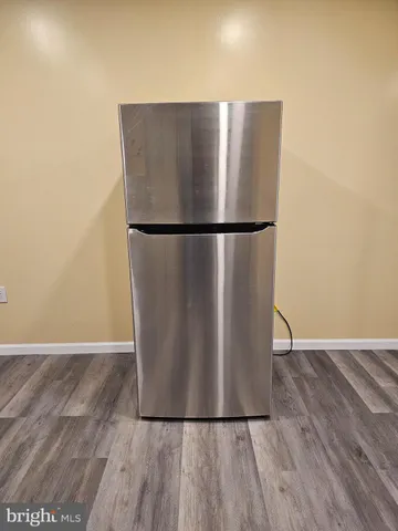 a view of a refrigerator in kitchen and an empty room with wooden floor