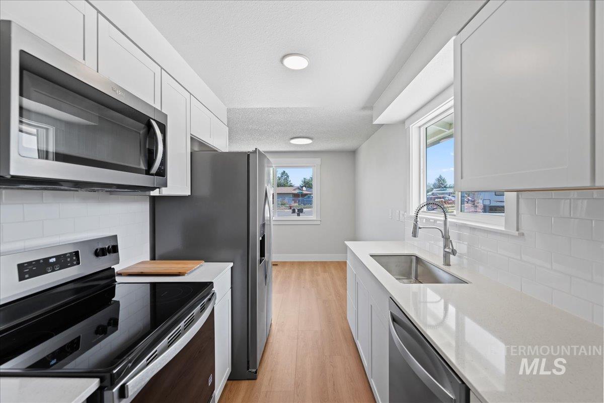 1309 West Maple Avenue Meridian, ID 83642 - Photo 10 of 50 Kitchen featuring decorative backsplash, stainless steel appliances, light wood-type flooring, light stone counters, and a textured ceiling