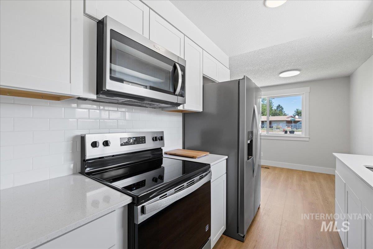 1309 West Maple Avenue Meridian, ID 83642 - Photo 11 of 50 Kitchen with appliances with stainless steel finishes, tasteful backsplash, white cabinets, light wood-type flooring, and a textured ceiling