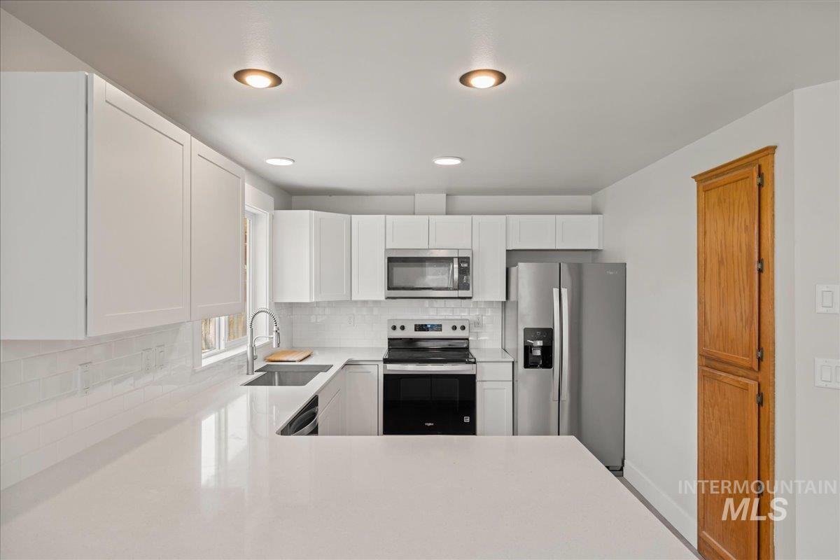 1309 West Maple Avenue Meridian, ID 83642 - Photo 31 of 50 Kitchen featuring stainless steel appliances, white cabinets, tasteful backsplash, light stone countertops, and recessed lighting
