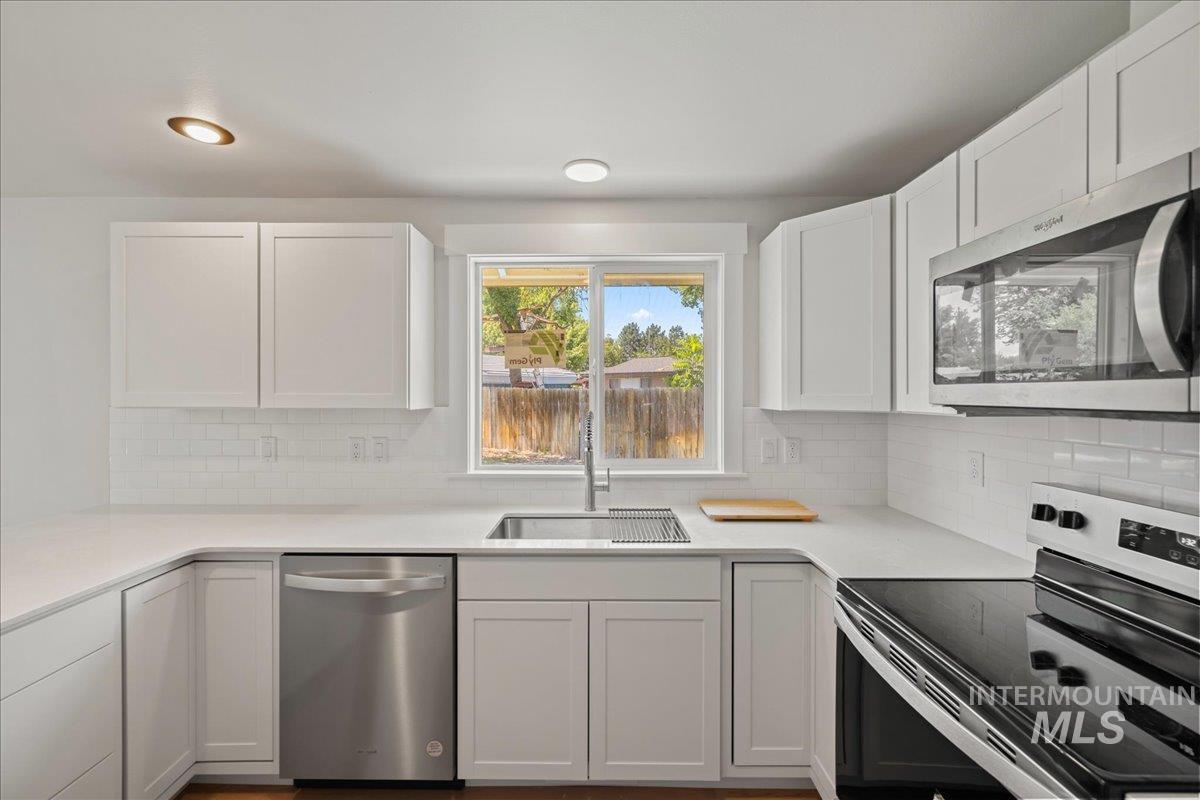 1309 West Maple Avenue Meridian, ID 83642 - Photo 32 of 50 Kitchen featuring stainless steel appliances, white cabinetry, tasteful backsplash, and light stone counters