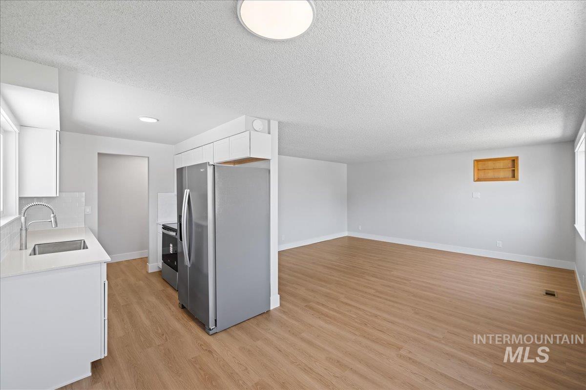 1309 West Maple Avenue Meridian, ID 83642 - Photo 49 of 50 Kitchen featuring appliances with stainless steel finishes, white cabinetry, light wood-style flooring, a textured ceiling, and open floor plan