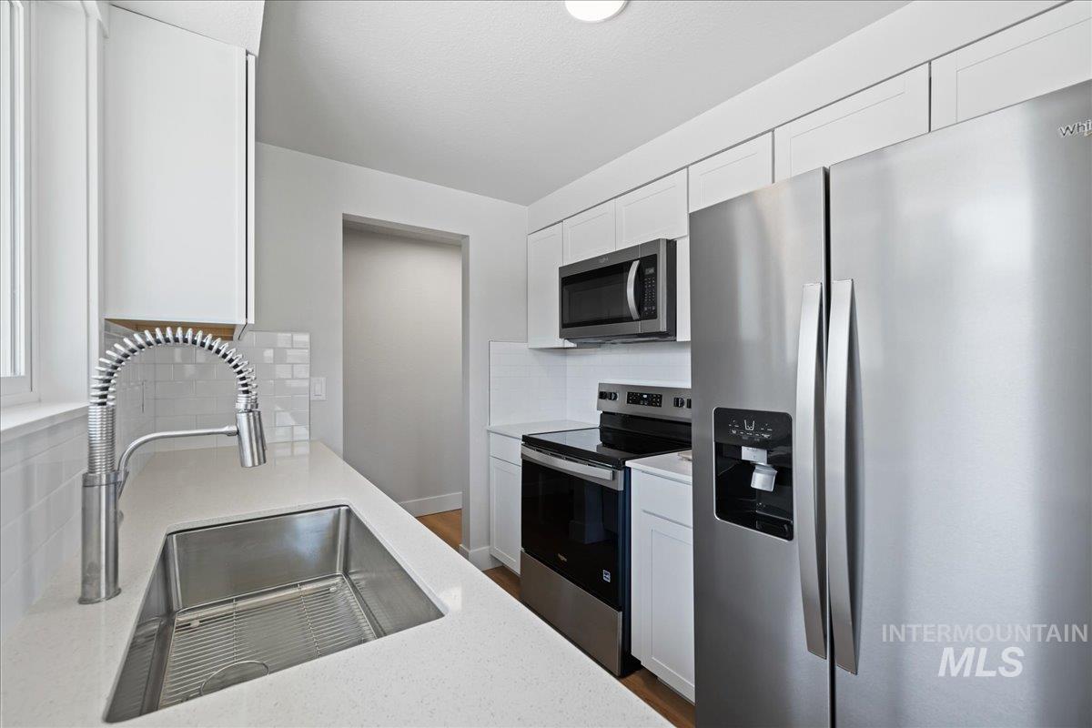 1309 West Maple Avenue Meridian, ID 83642 - Photo 9 of 50 Kitchen featuring stainless steel appliances, white cabinets, tasteful backsplash, dark wood-style floors, and light stone counters