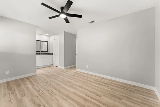 an empty room with wooden floor ceiling fan and kitchen view