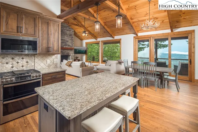 a kitchen with stainless steel appliances granite countertop a stove a refrigerator a kitchen island a dining table and chairs with wooden floor