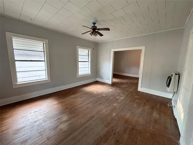 an empty room with wooden floor chandelier fan and windows