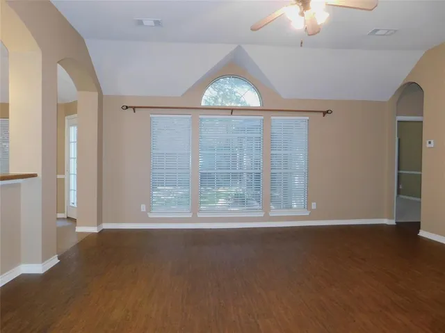 an empty room with wooden floor fan and windows