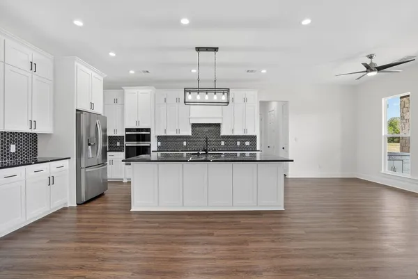 a large kitchen with granite countertop a large center island a sink dishwasher and a stove with wooden floor