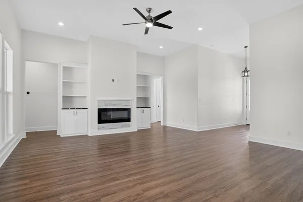 an empty room with wooden floor a ceiling fan a fireplace and windows