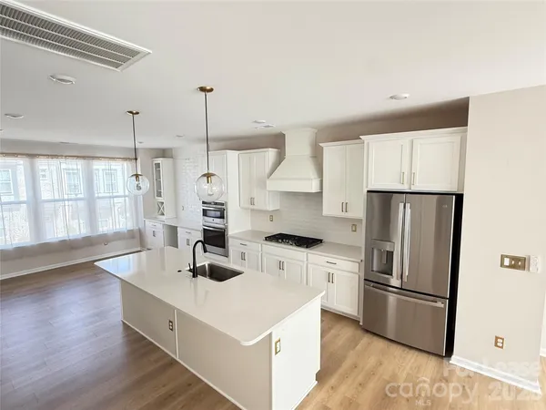 a kitchen with stainless steel appliances a stove a refrigerator a sink and white cabinets with wooden floor