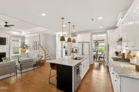 a living room with stainless steel appliances kitchen island granite countertop a table chairs and a view of living room