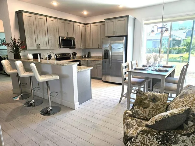 a kitchen with stainless steel appliances kitchen island granite countertop a refrigerator a stove a kitchen island a dining table and chairs with wooden floor