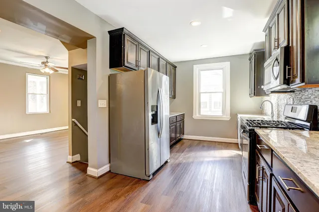 a kitchen with stainless steel appliances granite countertop a refrigerator a sink dishwasher a stove and white countertops with wooden floor