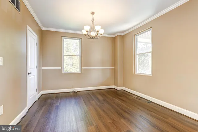 an empty room with wooden floor chandelier and windows