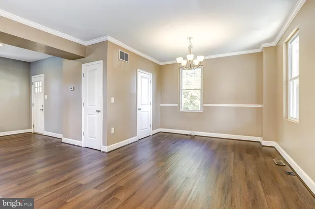 an empty room with wooden floor chandelier and windows
