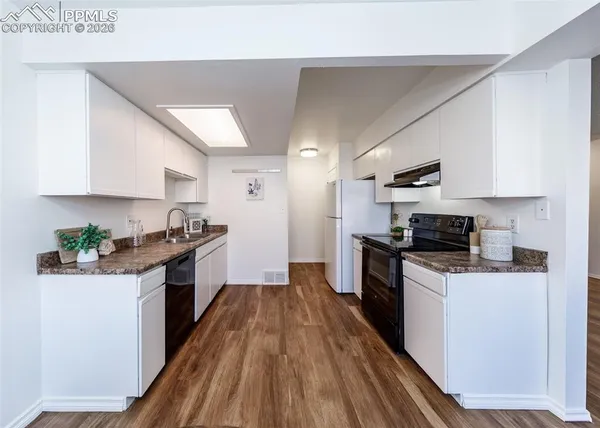 a kitchen with granite countertop a stove top oven a sink dishwasher and a refrigerator with wooden floor