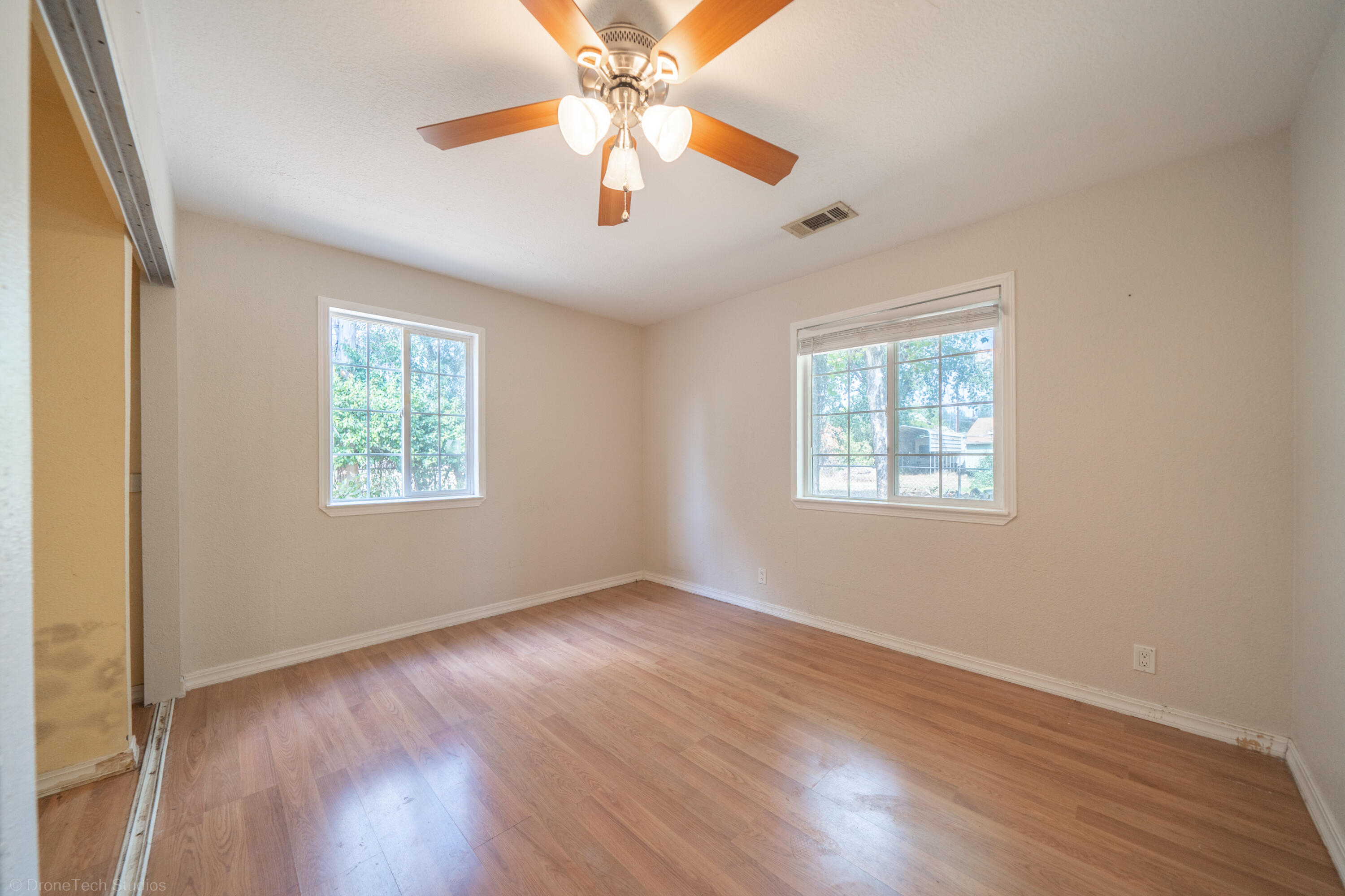 7673 Happy Valley Road Anderson, CA 96007 - Photo 20 of 72 an empty room with wooden floor chandelier fan and windows