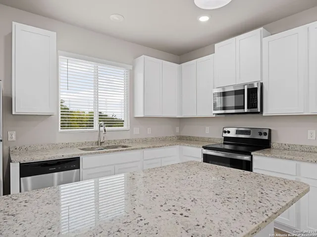 a view of kitchen with granite countertop refrigerator oven sink and white cabinets with wooden floor