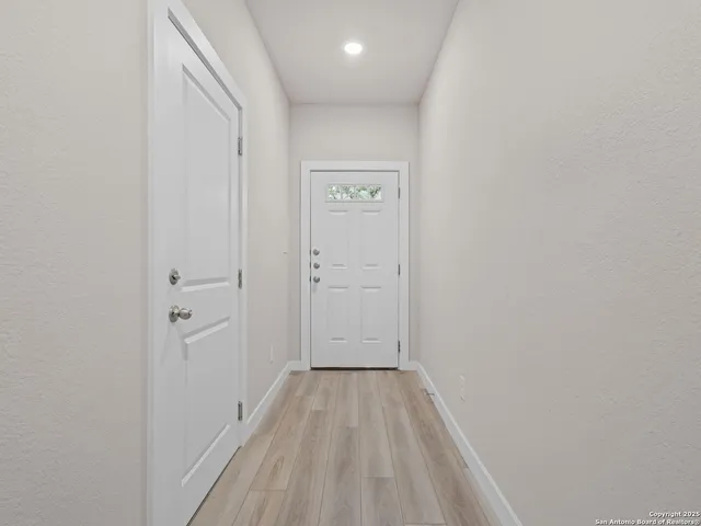 a view of an empty room with wooden floor and a kitchen
