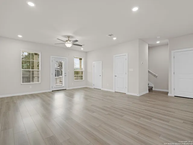 a view of an empty room and kitchen view with wooden floor