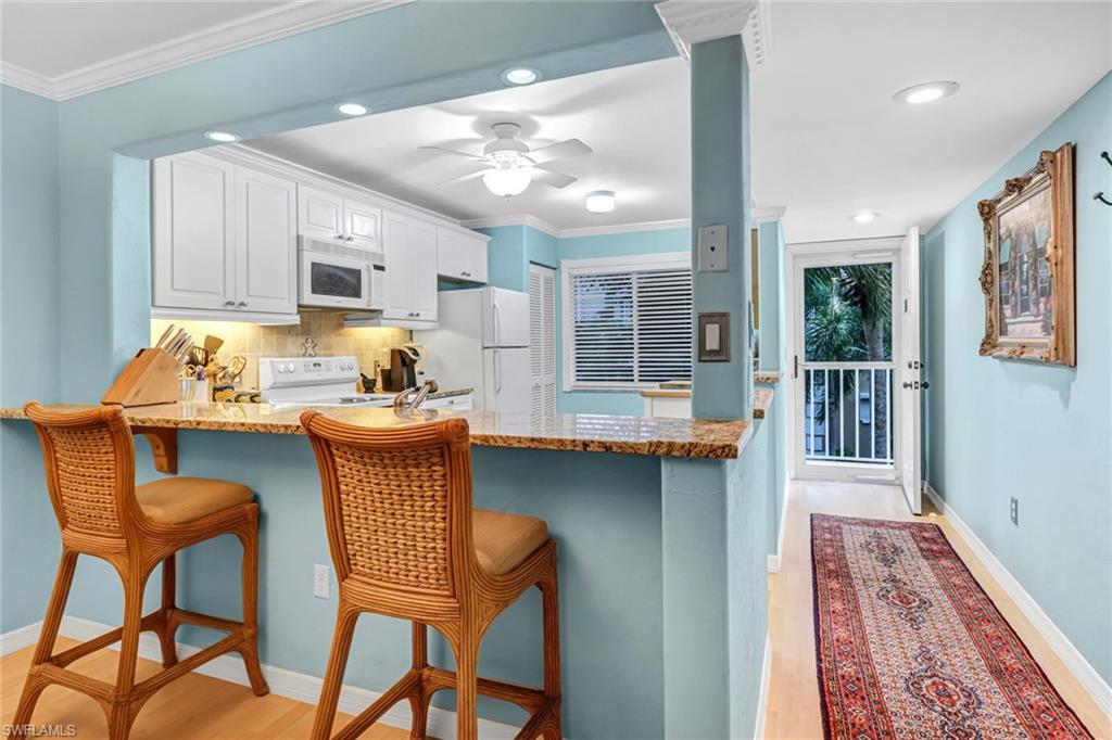 3041 Sandpiper Bay Circle, Unit H201 Naples, FL 34112 - Photo 2 of 25 Kitchen featuring light wood-style flooring, a kitchen bar, ornamental molding, light stone counters, and recessed lighting