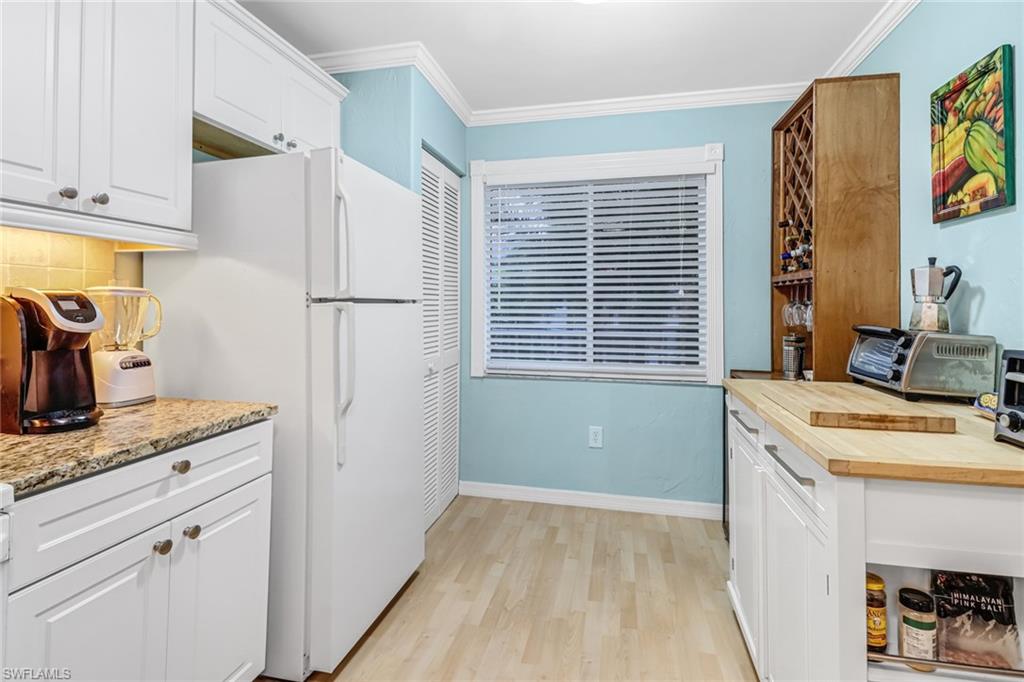 3041 Sandpiper Bay Circle, Unit H201 Naples, FL 34112 - Photo 4 of 25 Kitchen with white cabinets, ornamental molding, freestanding refrigerator, light wood finished floors, and decorative backsplash