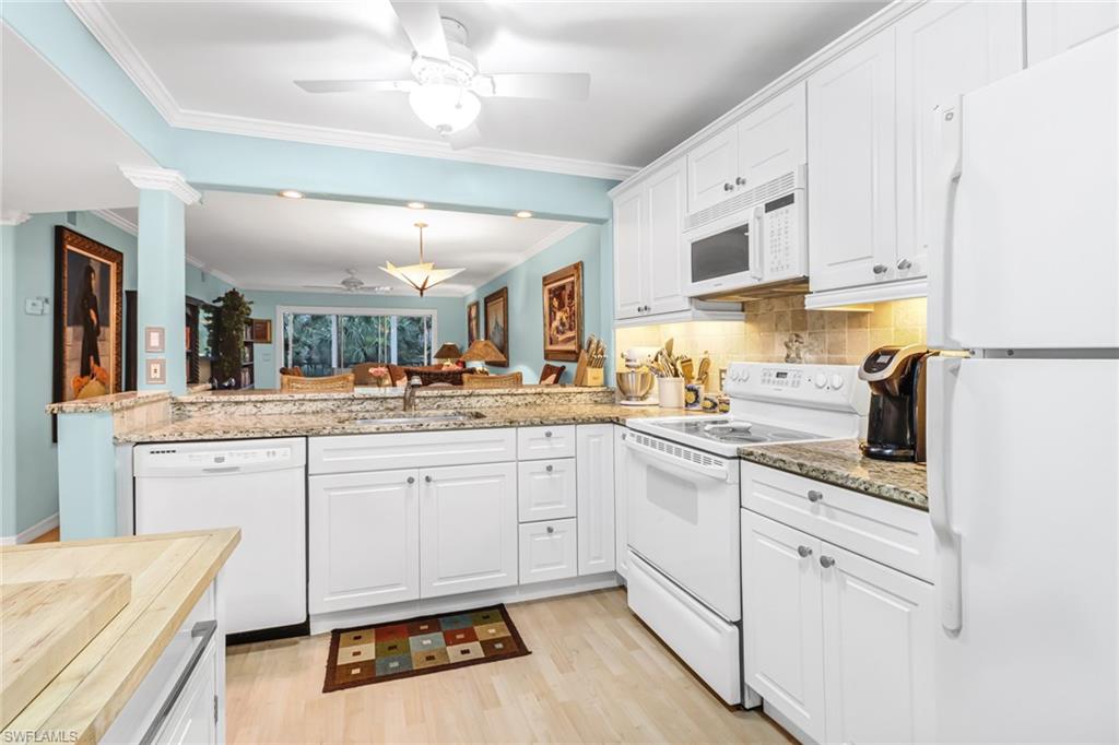 3041 Sandpiper Bay Circle, Unit H201 Naples, FL 34112 - Photo 5 of 25 Kitchen featuring white appliances, tasteful backsplash, white cabinetry, light wood finished floors, and crown molding