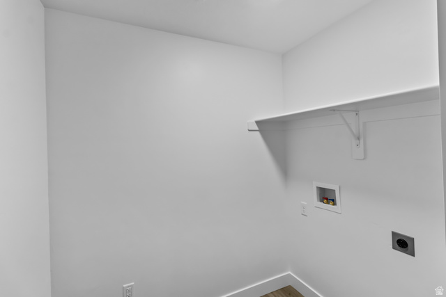 3014 South 265th Street West Logan, UT 84321 - Photo 17 of 25 Dedicated laundry area with a white wall-mounted shelf, electrical outlets, and plumbing connections, set against light-toned walls and wood-finish flooring