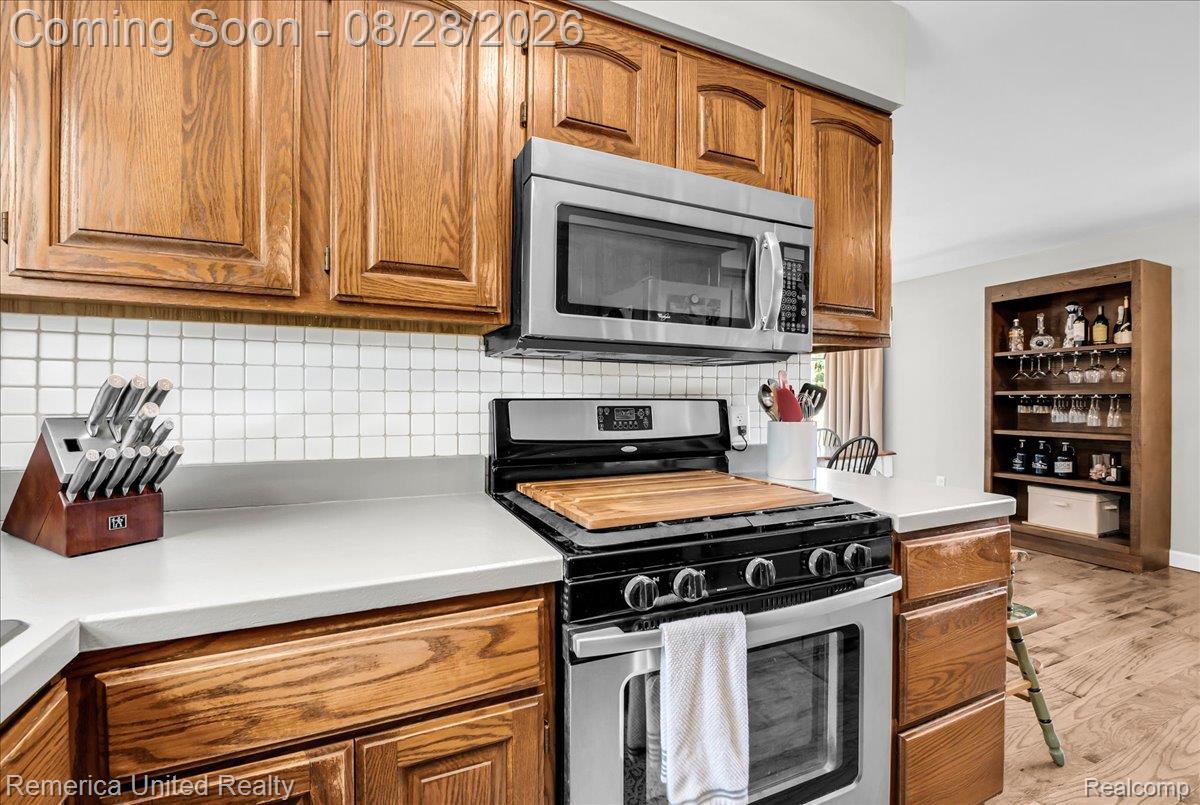 3687 Van Amberg Road Brighton, MI 48114 - Photo 13 of 56 Wood-finish cabinetry, stainless steel microwave, gas range, white square tile backsplash, and light-toned countertops