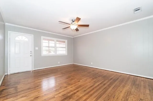 an empty room with wooden floor ceiling fan and windows
