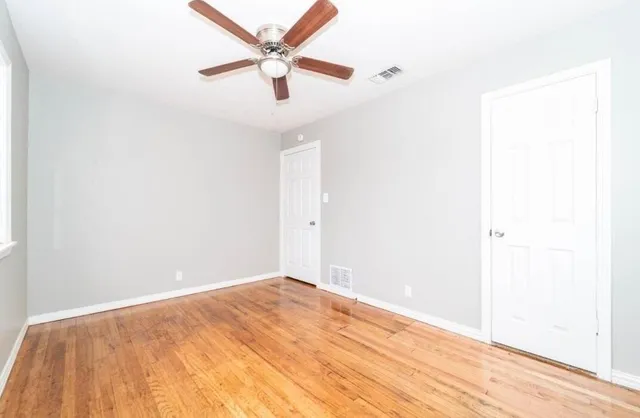 an empty room with wooden floor and a ceiling fan