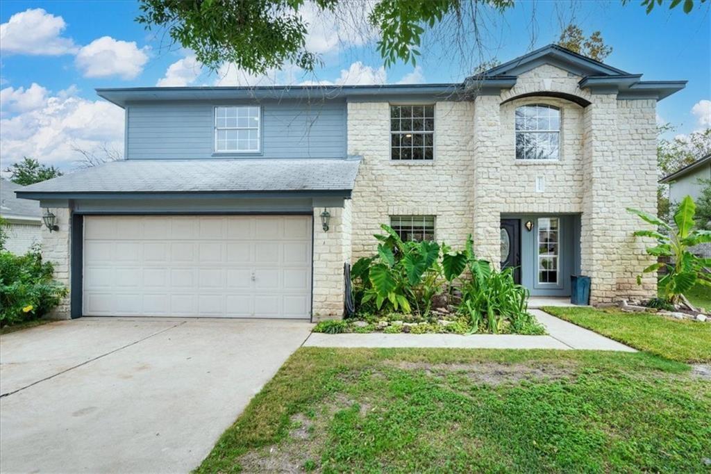 View of front of home with an attached garage, driveway, stone siding, and a front lawn