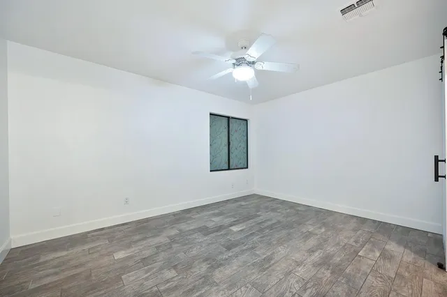a view of an empty room with wooden floor and a fan