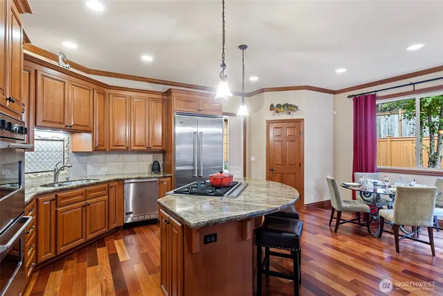 a kitchen with stainless steel appliances granite countertop a stove a sink dishwasher and a refrigerator with wooden floor