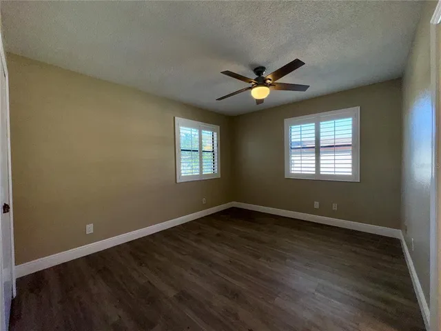 an empty room with wooden floor chandelier fan and windows