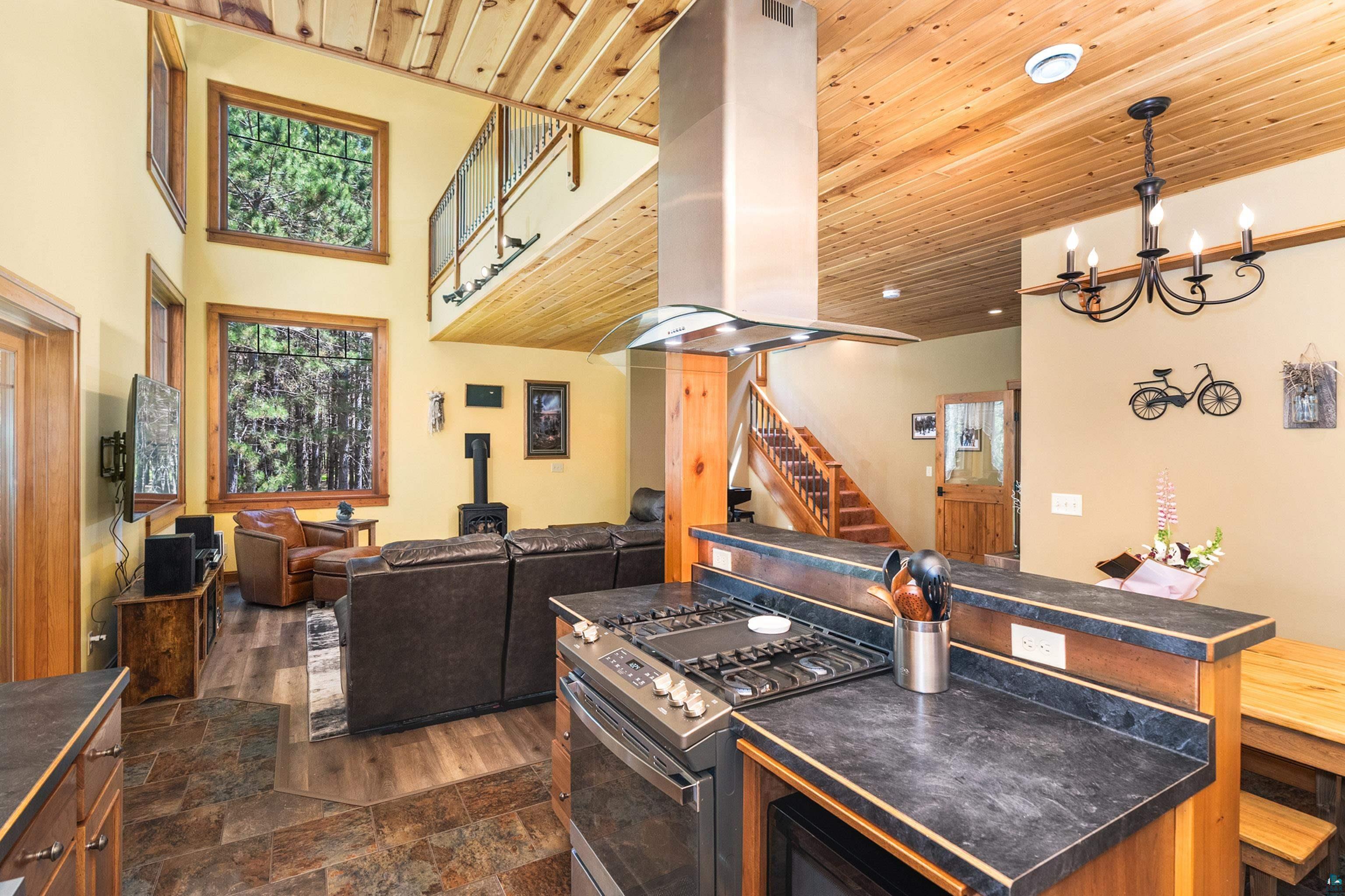 75 East Stark Road Esko, MN 55733 - Photo 23 of 87 Open-concept kitchen and living area featuring high vaulted ceilings with wood-paneling, a stainless steel range with overhead hood, dark countertops, and large windows