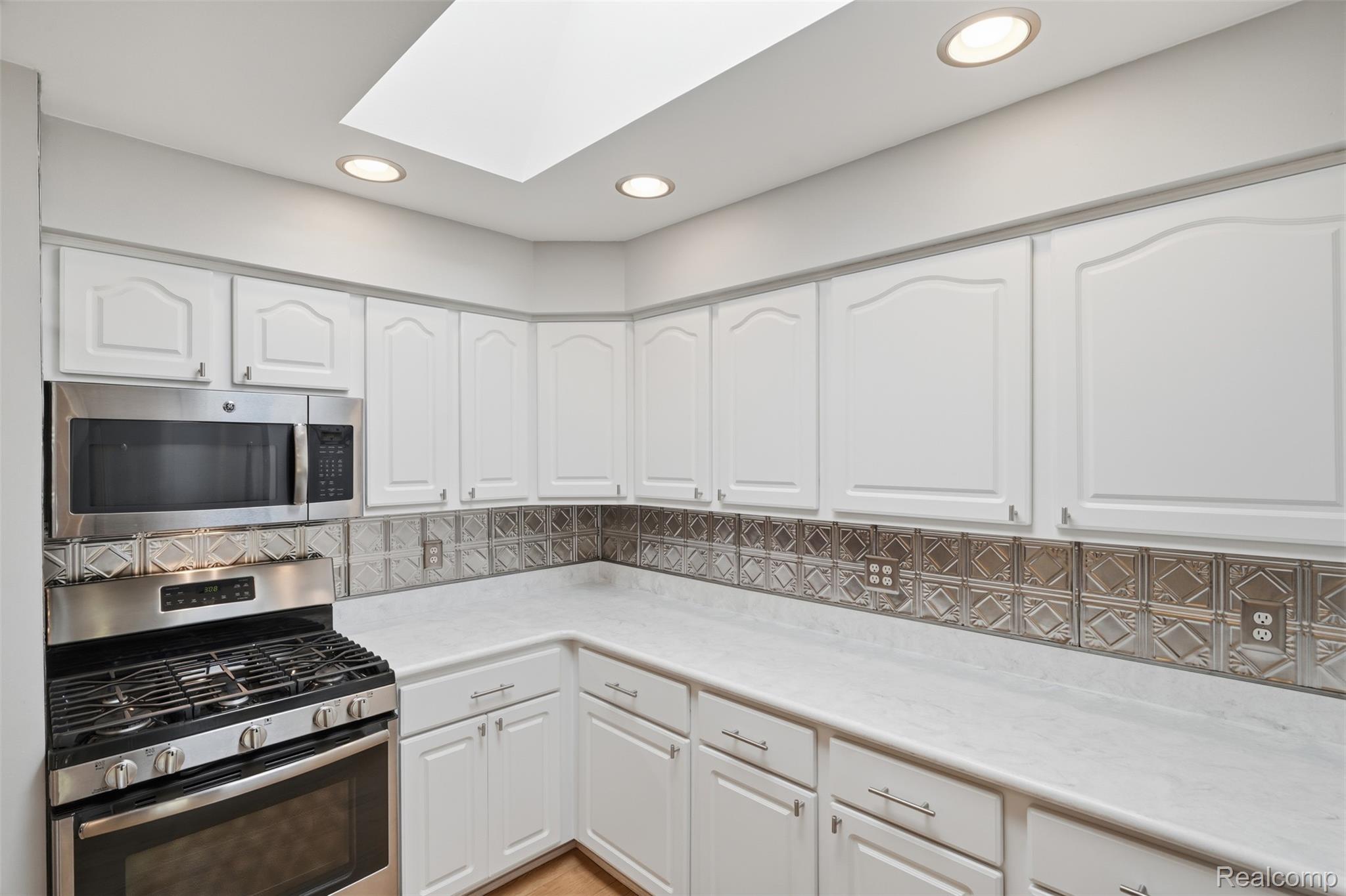 1087 Collingwood Drive Rochester, MI 48307 - Photo 12 of 56 Kitchen featuring white cabinetry, stainless steel appliances, a patterned tile backsplash, recessed lighting, and a skylight