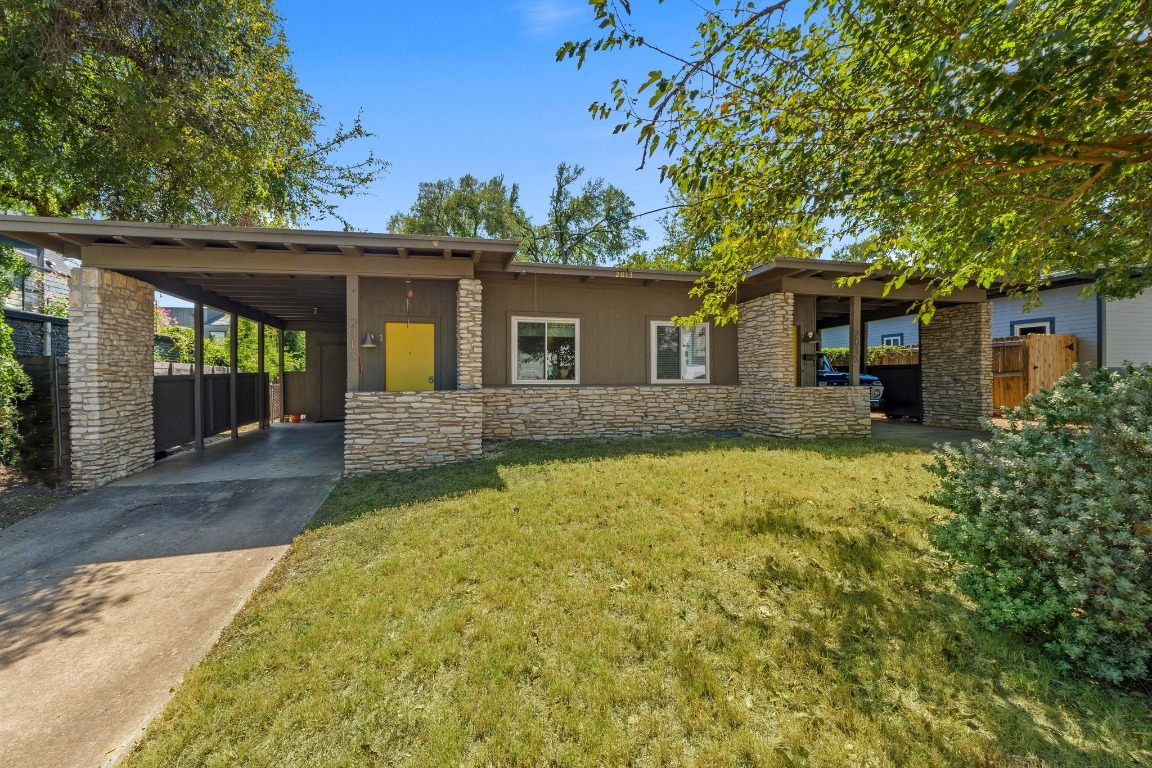 View of front facade with stone siding, an attached carport, concrete driveway, and a patio
