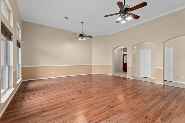 a view of an empty room with wooden floor and a ceiling fan