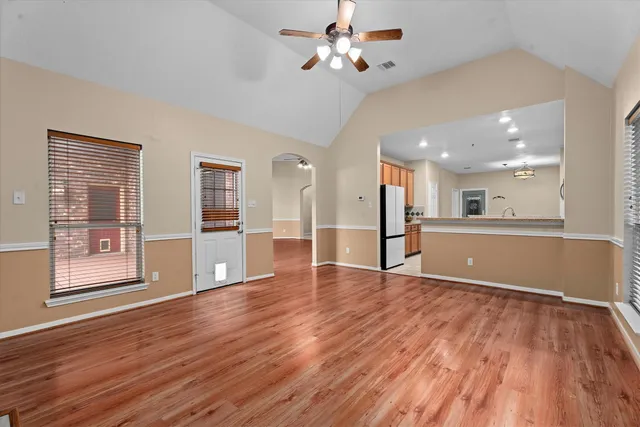 a view of an empty room with wooden floor and a kitchen