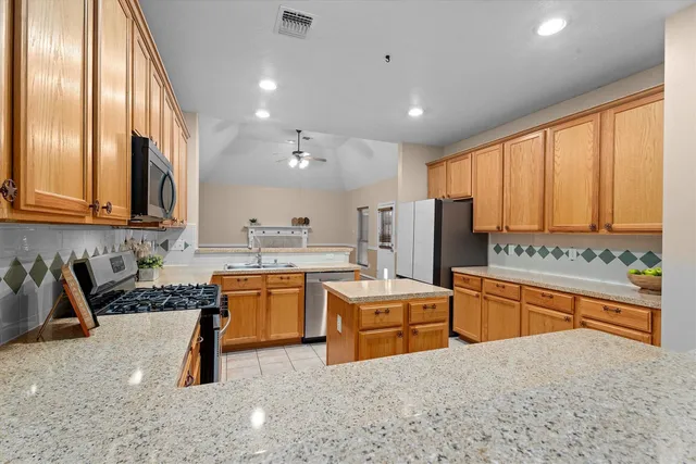 a kitchen with stainless steel appliances granite countertop a refrigerator a sink dishwasher a stove and white countertops with wooden floor