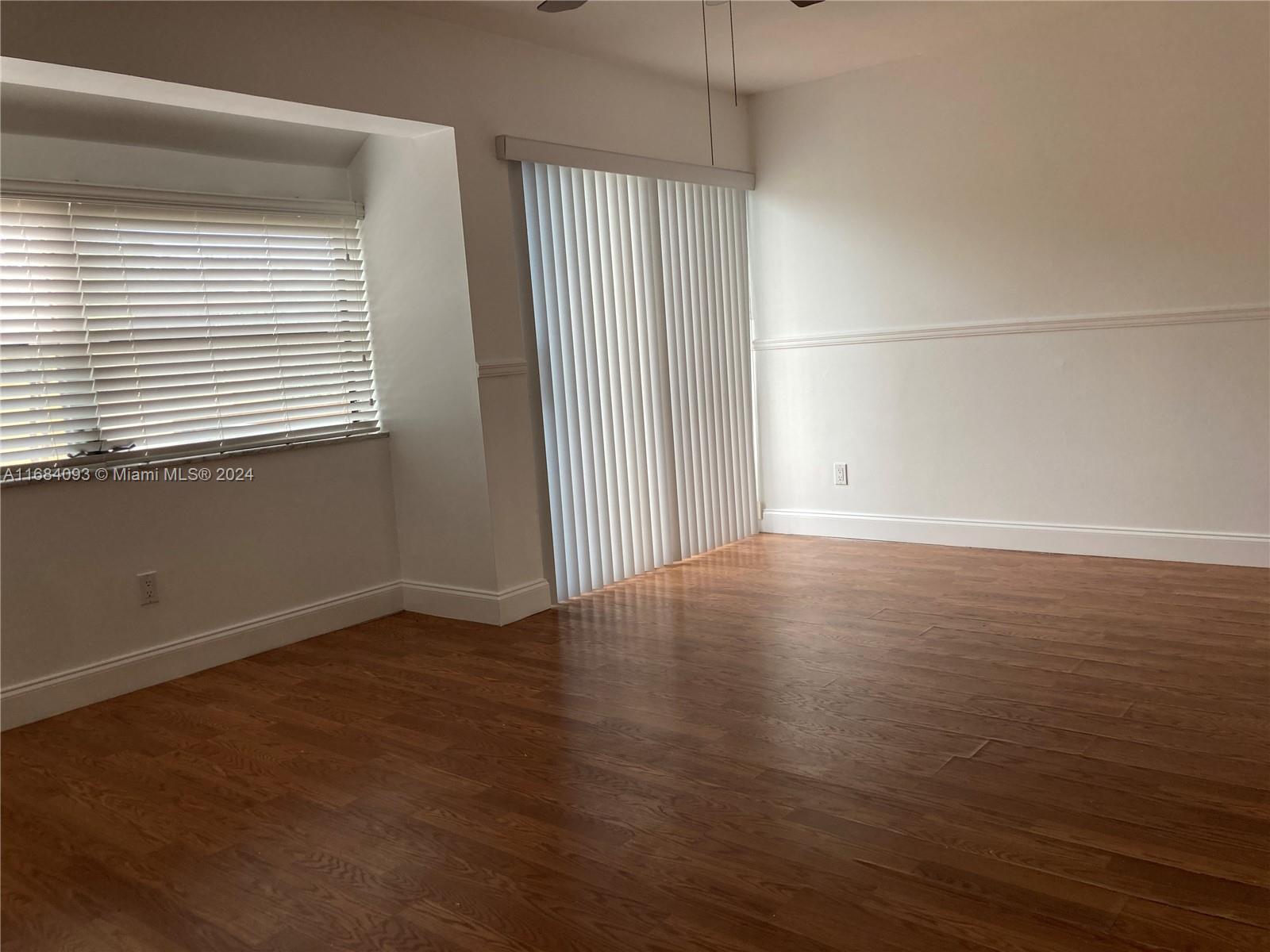 13731 Southwest 84th Street, Unit E Miami, FL 33143 - Photo 16 of 19 an empty room with wooden floor and windows with curtains