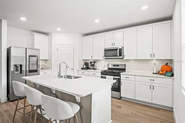 a kitchen with stainless steel appliances a sink stove refrigerator and white cabinets with wooden floor