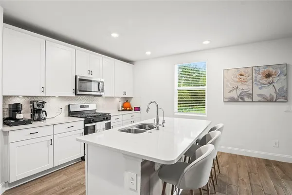 a kitchen with stainless steel appliances a stove a sink a refrigerator white cabinets and wooden floor