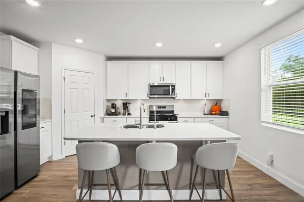 a kitchen with stainless steel appliances a dining table chairs refrigerator and sink