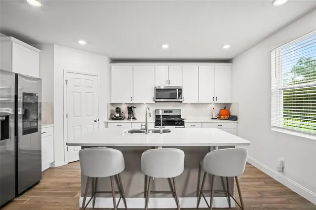 a kitchen with stainless steel appliances a dining table chairs refrigerator and sink